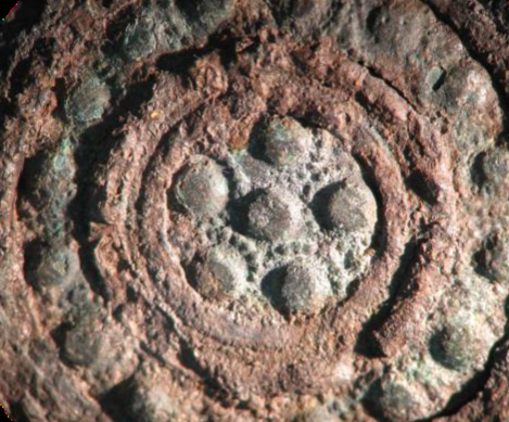 la restauración iniciada de uno de los nielados de cobre de la vaina del puñal de la tumba 109 (SECYR 436), donde se ha retirado parcialmente la película de óxidos de hierro que cubría la decoración de cobre (ampliación 20×)